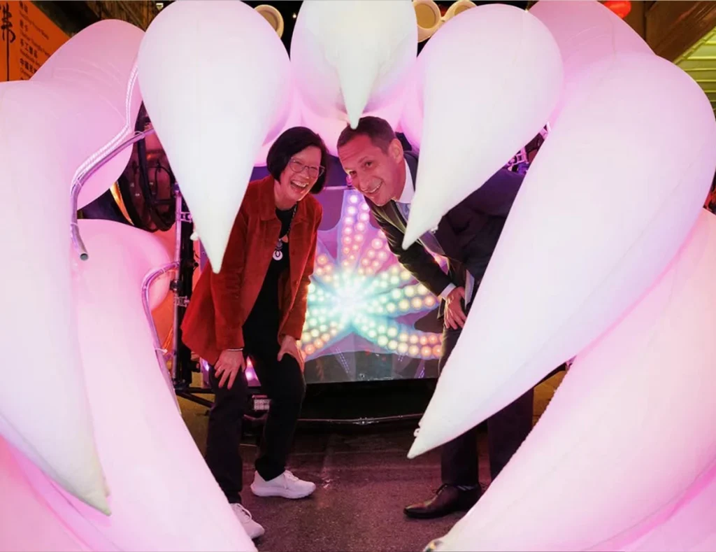 daniel-lurie-joanne-lee-the-cuttlefish-super-flex-sf-by-mel.movs San Francisco Mayor Daniel Lurie and arts leader Joanne Lee smiling inside the glowing tentacles of The Cuttlefish, a large-scale luminous kinetic inflatable art installation at the Super Flex festival.